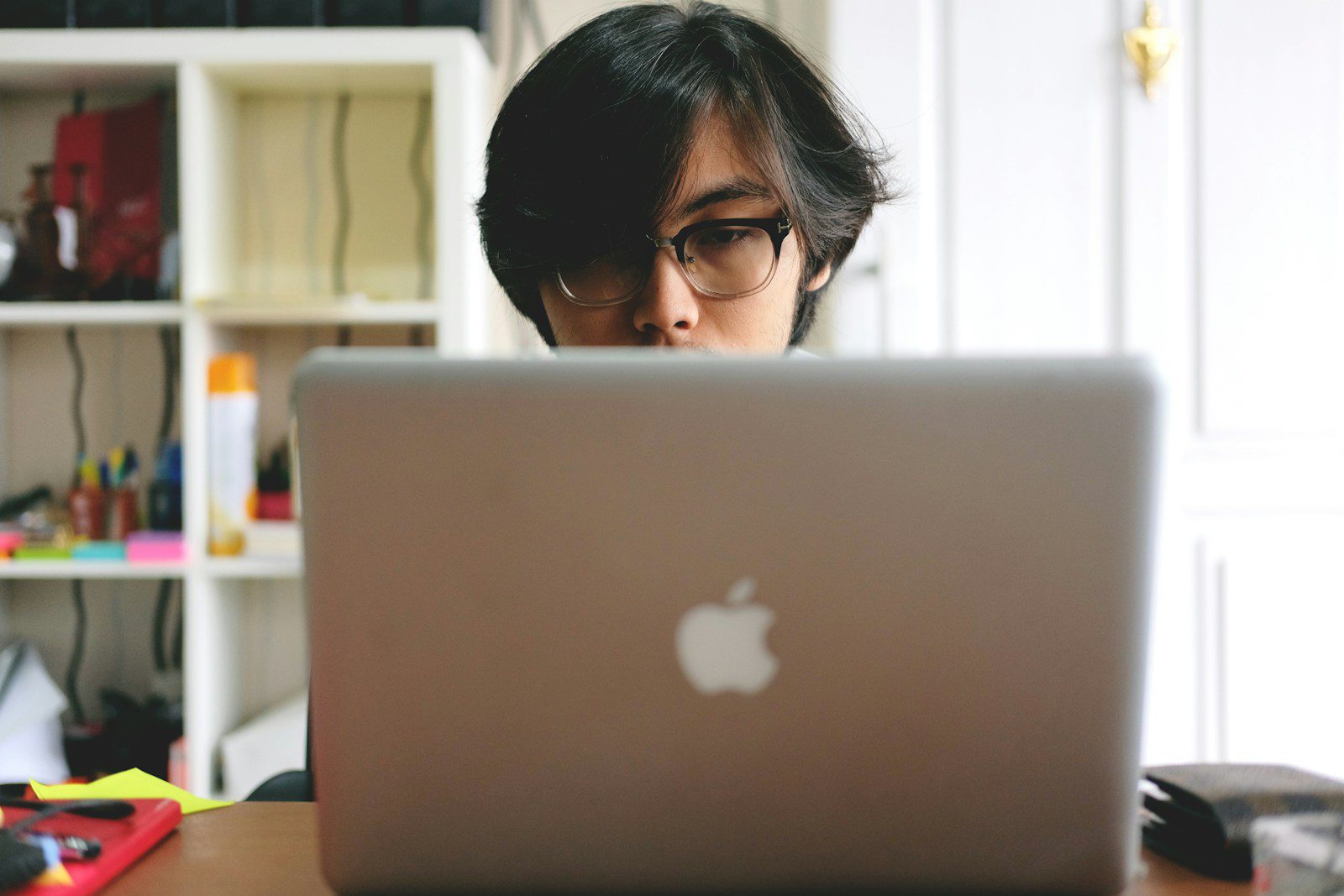 man wearing eyeglasses while using silver Macbook near wooden cubby shelf inside room - ADHD task paralysis
